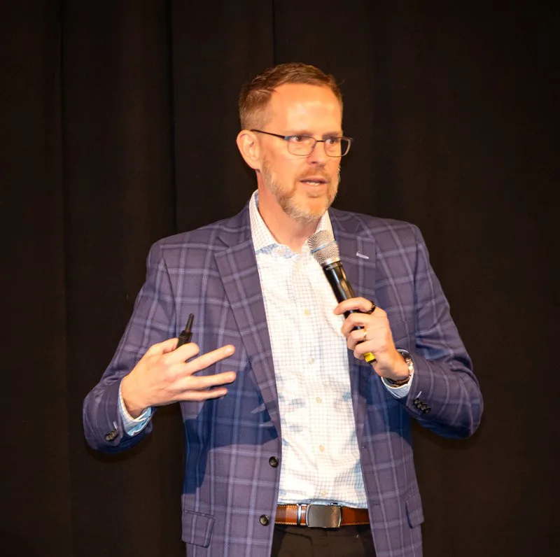 Greg Adgate speaking with a microphone at an industry event